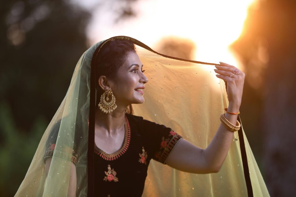 Woman with traditional earrings and veil smiling in sunset outdoors.
